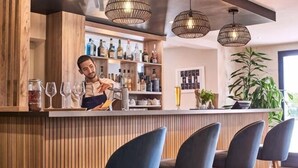 A bar area with wooden paneling, a bartender, and bar stools. - Kyriad Sens (Sens)