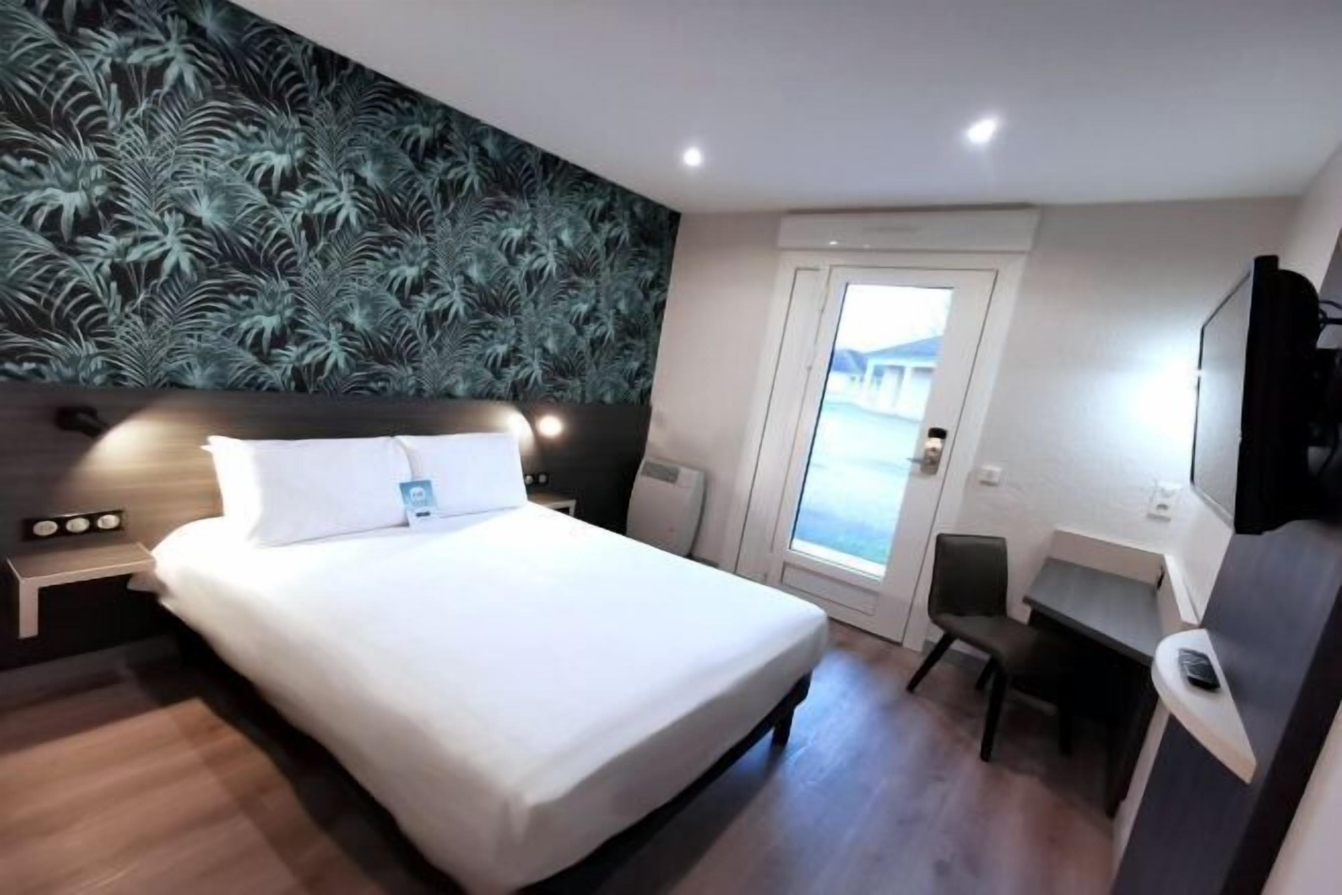 A modern hotel room with a large bed, a desk, and a view of the outside.