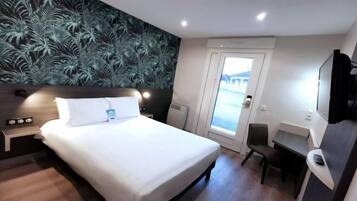 A modern hotel room with a large bed, a desk, and a view of the outside.