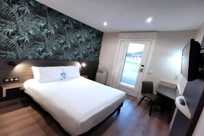 A modern hotel room with a large bed, a desk, and a view of the outside. - Kyriad Sens (Sens)