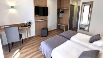 A modern hotel room with a wooden floor, a desk with a chair, a flat-screen TV, a wardrobe, and two beds.