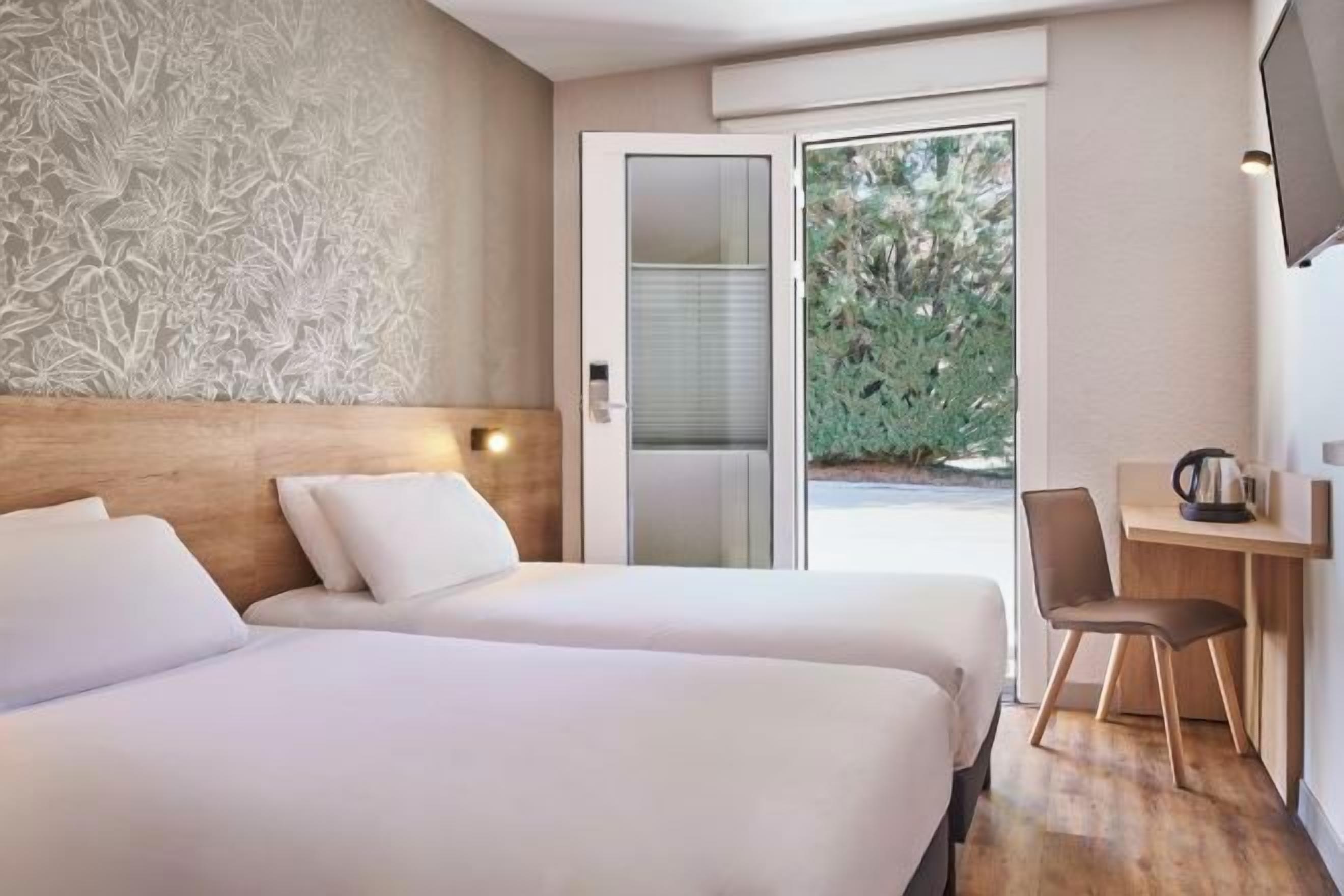 A hotel room with two beds, a desk, and a television.