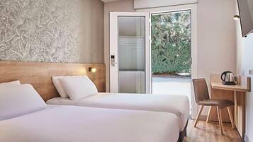 A hotel room with two beds, a desk, and a television.