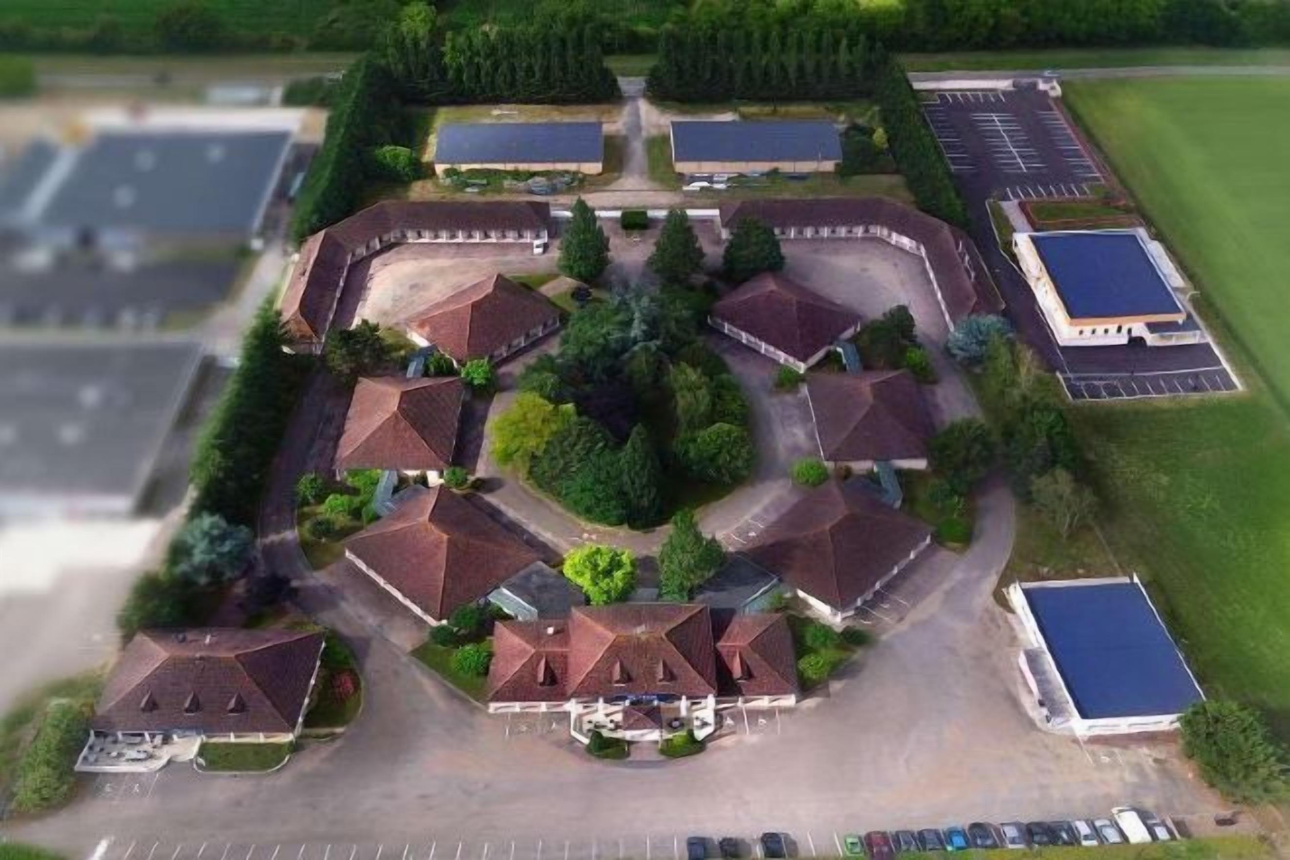 Luchtbeeld van een hotel met meerdere gebouwen, parkeerplaatsen en groene zones.