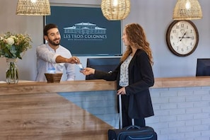 Un comptoir d’accueil avec une horloge et une enseigne indiquant « LES TROIS COLONNES ».