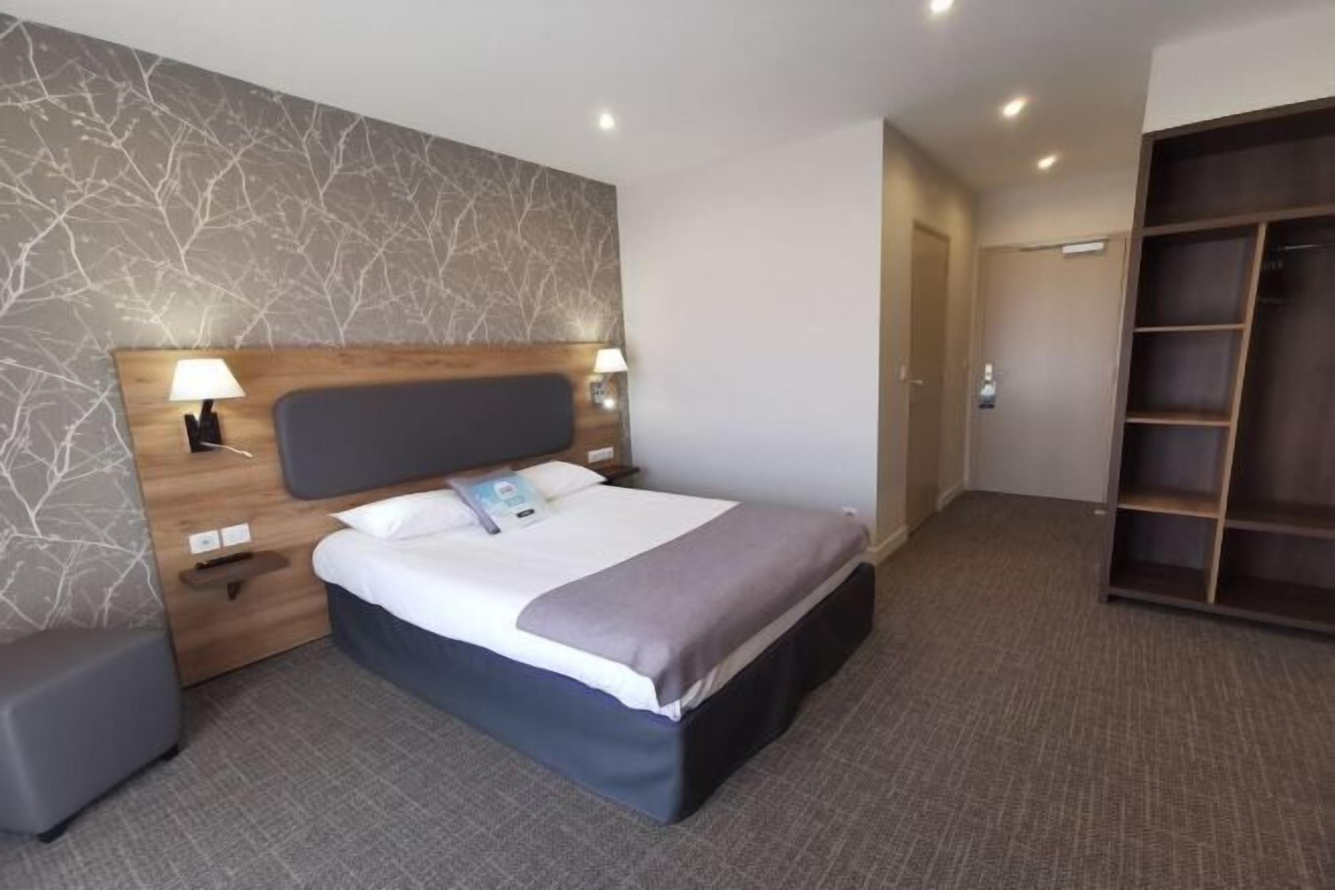 A hotel room with a bed, bedside tables, a wardrobe, and a wall with a tree branch pattern.