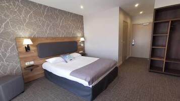 A hotel room with a bed, bedside tables, a wardrobe, and a wall with a tree branch pattern.