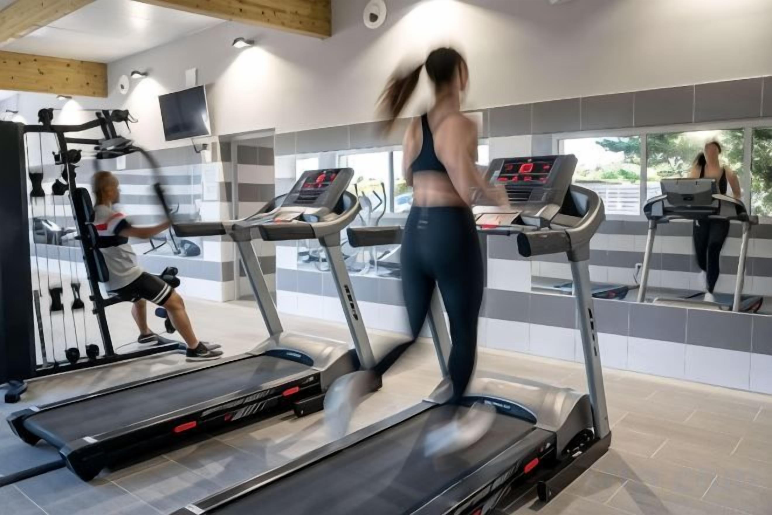 A gym with treadmills, exercise equipment, and a mirrored wall.