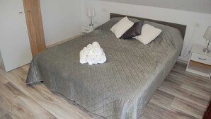 Un lit bien fait, avec une couverture grise, deux oreillers et des serviettes enroulées posées sur le lit.