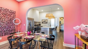 A modern kitchen with a stainless steel refrigerator, a dining area with a glass table and black chairs, and a pink wall with a mosaic design. - 36 Guests on Music Row Bachelorette Suites + Glam Room 5 Minutes to Downtown (Nashville)