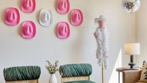 A room with a wall adorned with hats, a mannequin with a feathered hat, two green-striped sofas, a white vase with flowers, and a lamp on a side table. - 36 Guests on Music Row Bachelorette Suites + Glam Room 5 Minutes to Downtown (Nashville)