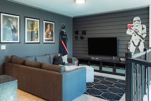 A modern living room with a large flat-screen TV, a brown sectional sofa, and Star Wars-themed decorations including a Stormtrooper cutout and framed posters. - Fantasy Stay in 5 bed at Storey Lake (Kissimmee)