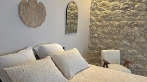 A bedroom with a large bed, two decorative wall hangings, a stone wall, and a small chair.