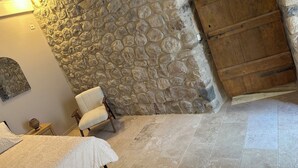 A stone wall, wooden door, and a chair in a room with tiled flooring.
