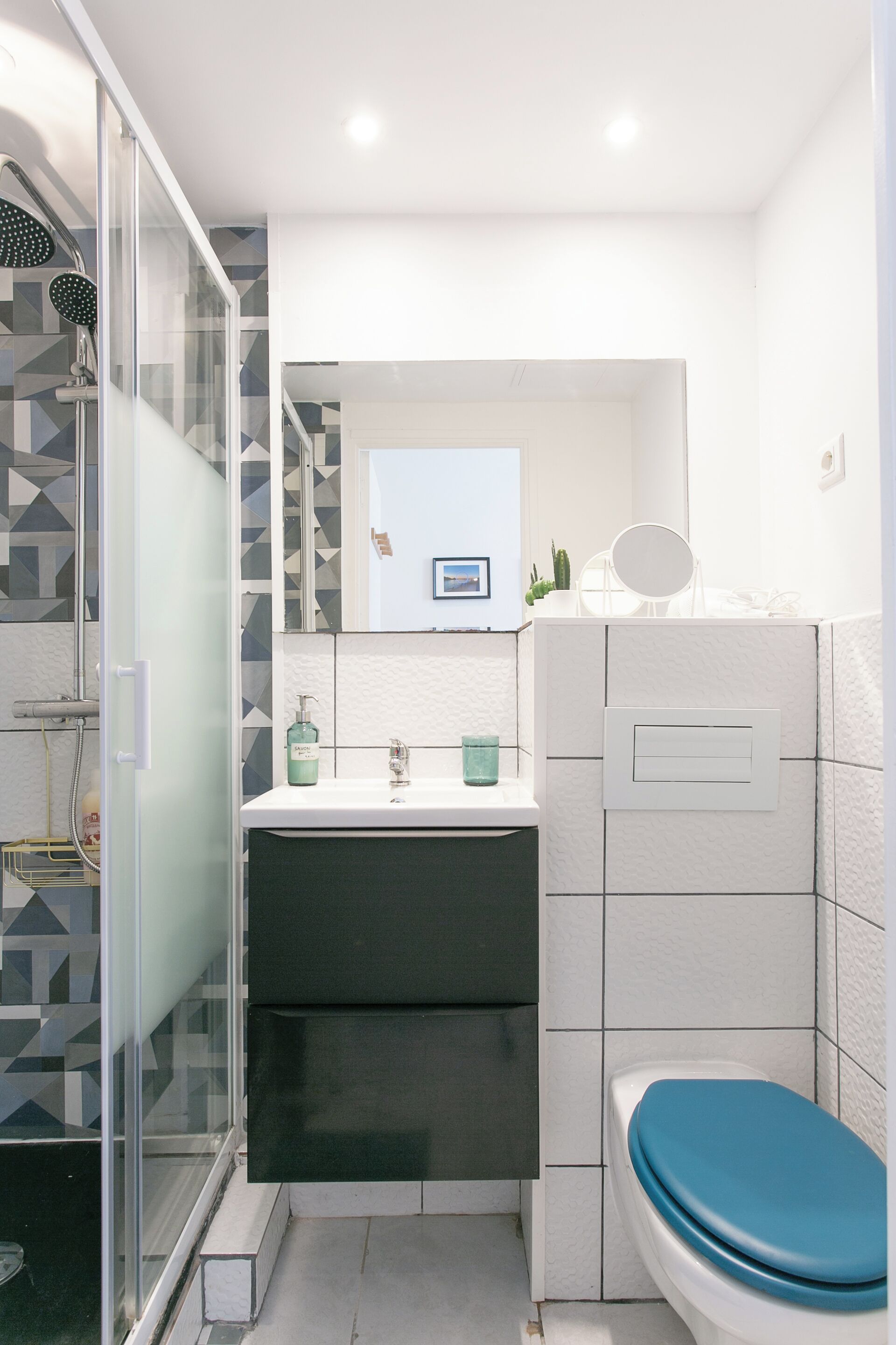 Un baño moderno con cabina de ducha de vidrio, un lavabo blanco con espejo y un inodoro con asiento azul.