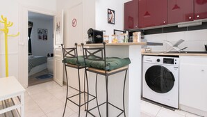 Une cuisine compacte équipée d’un lave-linge, d’une machine à café et d’un tabouret de bar.