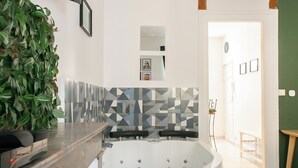 Une salle de bain moderne avec une baignoire sur pieds, un grand miroir et une plante verte posée sur le comptoir.