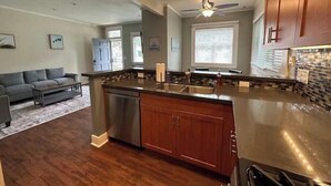 A modern kitchen with a central island, stainless steel appliances, wooden cabinets, and a ceiling fan. - Sunny condo across the Bay in Pacific Beach! (San Diego)