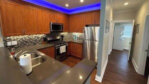 A modern kitchen with wooden cabinets, stainless steel appliances, and a blue accent wall. - Sunny condo across the Bay in Pacific Beach! (San Diego)