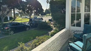 A porch with a stone wall and a view of a street with parked cars and trees. - Sunny condo across the Bay in Pacific Beach! (San Diego)