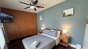 A bedroom with a bed, wooden wardrobe, ceiling fan, bedside lamps, and a painting on the wall. - Sunny condo by the Bay! [unit B] (San Diego)
