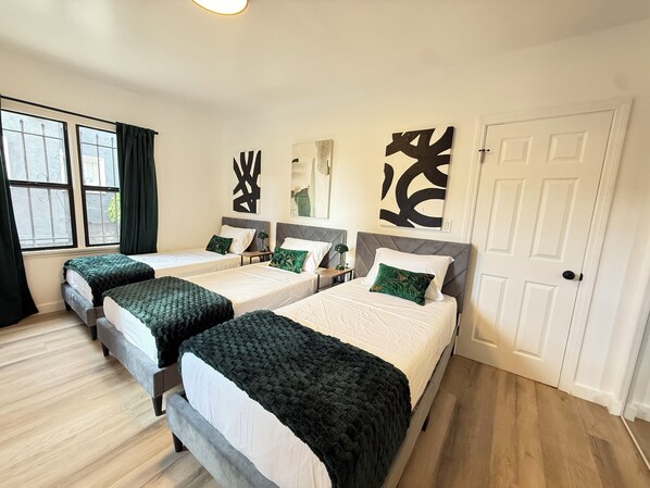 A hotel room with three beds, a large window with curtains, and abstract wall art. - Modern 2Br + Sofa Bed + 2Bth in Miracle Mile (Los Angeles)