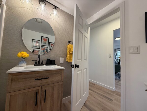 A bathroom with a wooden vanity, a round mirror, and a vase of yellow flowers.