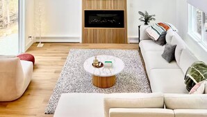 A modern living room with a wooden accent wall, a ceiling fan, a large painting, a fireplace, and a white sofa.