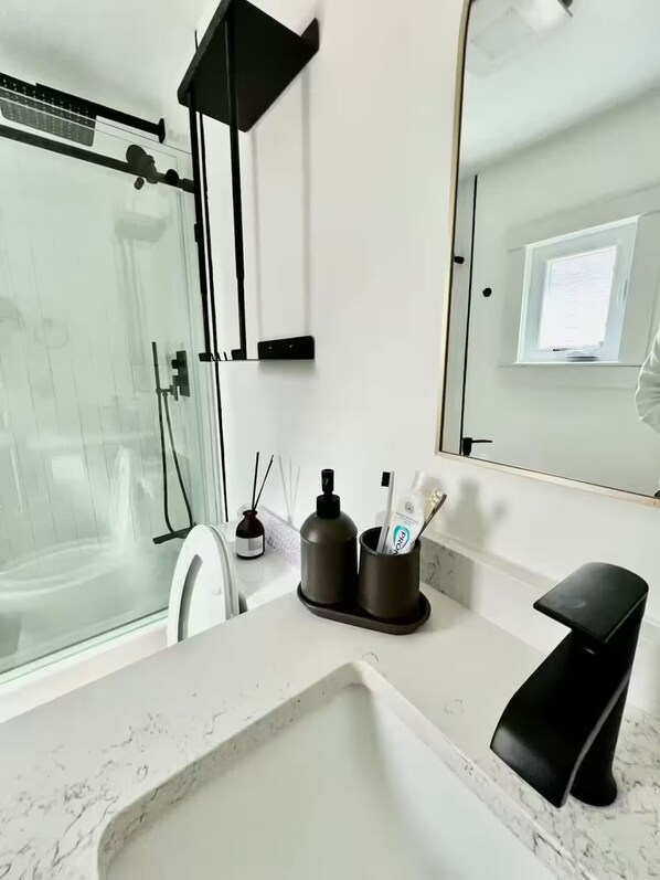 Un baño moderno con cabina de ducha de vidrio, un lavabo blanco con grifo negro y un espejo sobre el lavabo.