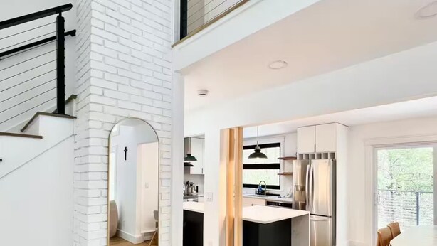 A modern kitchen with a central island, a dining area with a table and chairs, and a staircase with a black railing.