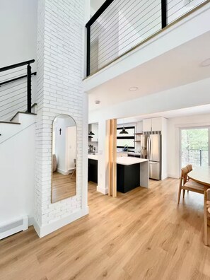 Una cocina moderna con una isla central, un comedor con mesa y sillas, y una escalera con barandilla negra.
