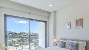 Une chambre avec une grande porte-fenêtre coulissante donnant sur un balcon, un lit avec deux oreillers et deux tableaux encadrés au mur.