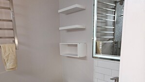 A bathroom with a toilet, a sink, and a mirror. There are shelves above the sink and a towel hanging on the wall.