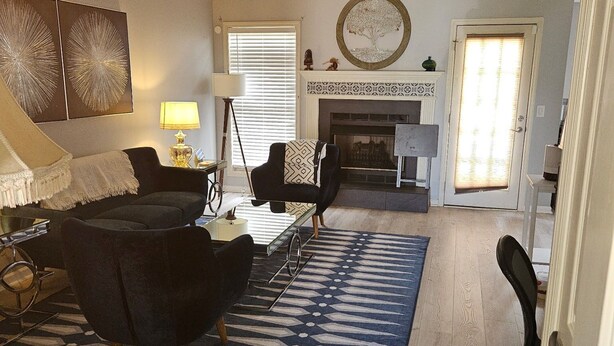 A living room with a ceiling fan, a fireplace, and a large window with blinds.