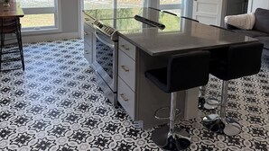 Una cocina moderna con una isla central, ventanas amplias y un suelo estampado.