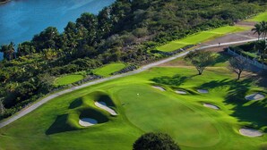 An aerial view of a golf course with sand bunkers, a water body, and dense vegetation.