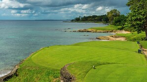 A coastal golf course with a view of the ocean and a cloudy sky.