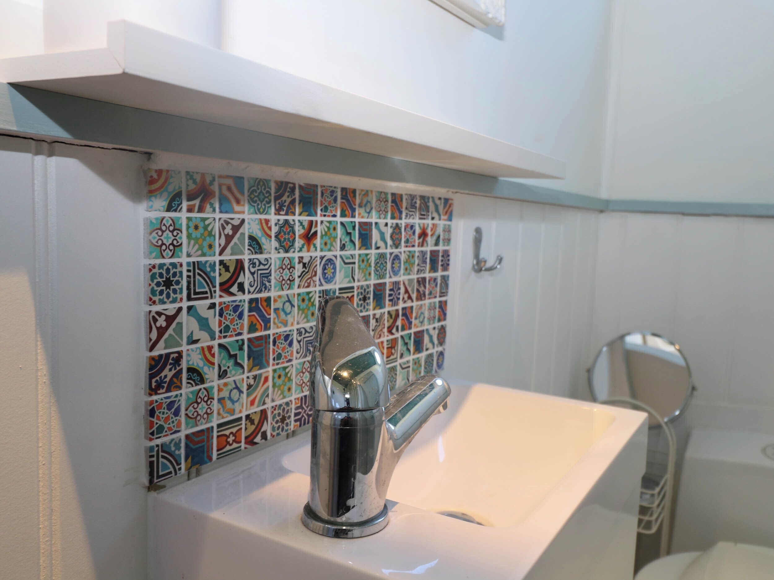 Une salle de bain avec un lavabo blanc, un robinet chromé et un pare-éclaboussures carrelé aux motifs colorés.