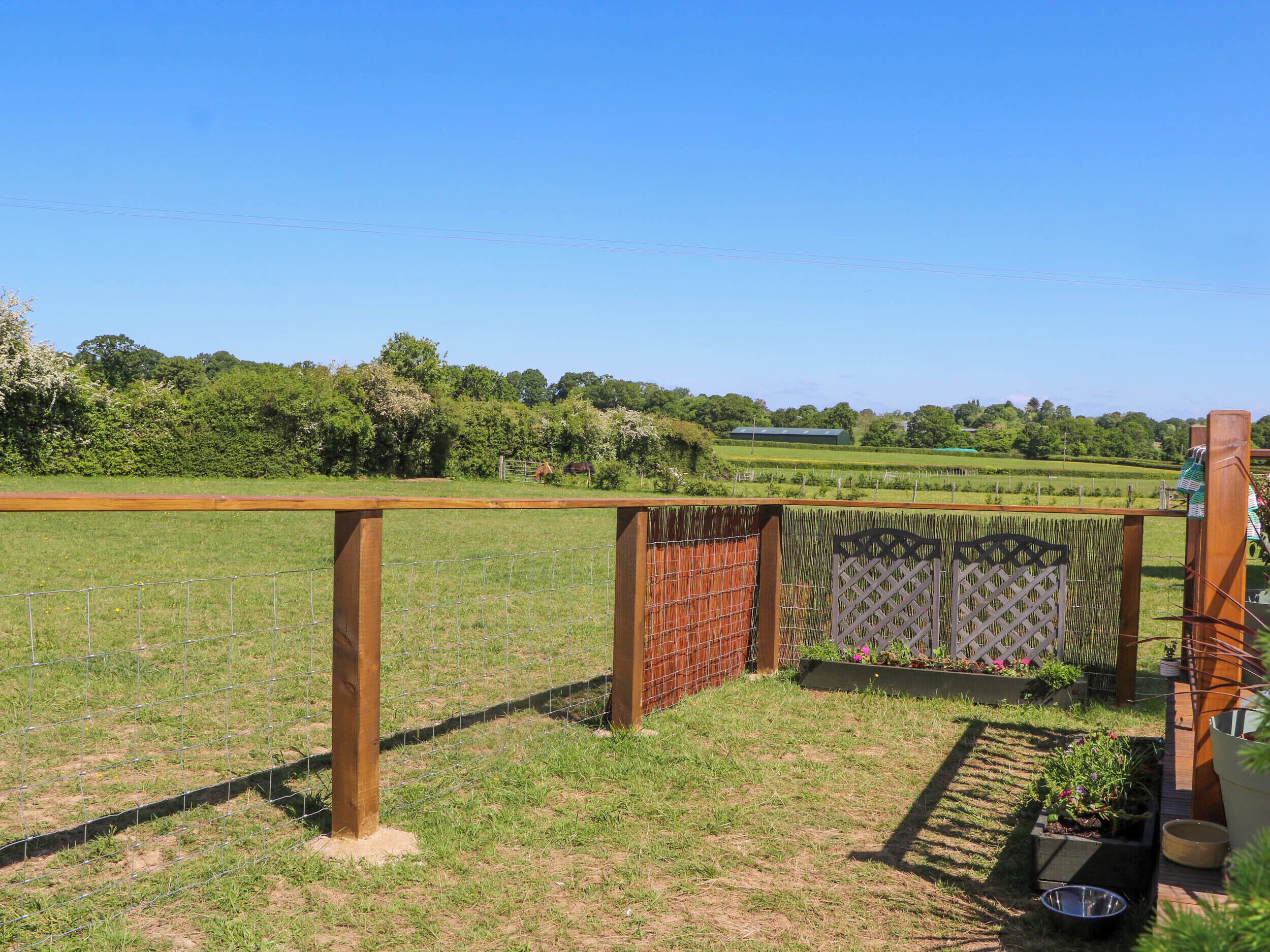 A fenced outdoor area with a wooden gate, a metal fence, and a grassy field.