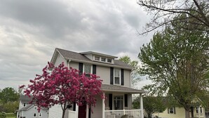 A two-story house with a porch and a tree with pink flowers. - The Bly House (Fulton)