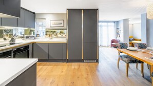 Et moderne køkken med en central ø, indbyggede apparater og et spiseområde med et træbord og stole.