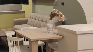 A modern dining area with a wooden table, white chairs, a beige sofa, and a white pendant light. - Cozy apartment in heart of Santa Tecla (Santa Tecla)