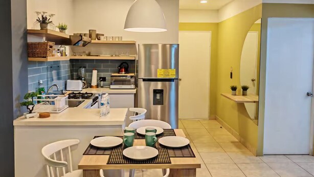A modern kitchen with a central island, stainless steel appliances, and a dining area with a table set for four. - Cozy apartment in heart of Santa Tecla (Santa Tecla)