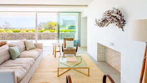 A modern living room with a sofa, armchairs, a glass coffee table, and a fireplace. - Heath House, Thorpeness (Thorpeness)
