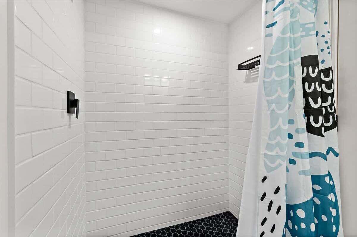 Eine Dusche mit weiß gefliesten Wänden und einem schwarz-weißen Duschvorhang.