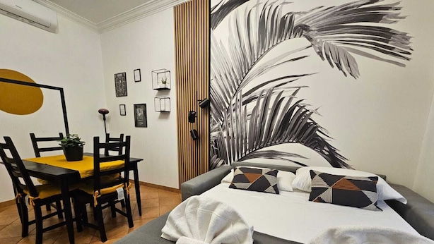 A hotel room with a bed, a dining table with chairs, a wall-mounted air conditioner, and framed pictures on the wall. - Giulio's Apartment - by Be Your Home (Rome)
