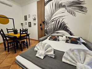 Een hotelkamer met een bed, een eettafel met stoelen, een wandairco en ingelijste foto’s aan de muur.