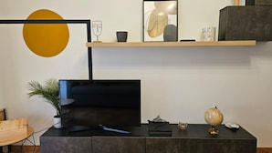 A modern living room with a flat-screen TV, a wooden coffee table, a potted plant, a globe, and a minimalist shelf with decorative items. - Giulio's Apartment - by Be Your Home (Rome)
