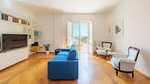 A modern living room with a blue sofa, a flat-screen TV, and a bookshelf. - Terrazza Aphrodite - Two Bedroom Apartment, Sleeps 5 (Salerno)