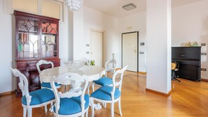A dining area with a white round table, blue cushioned chairs, a wooden cabinet with glass doors, and a black cabinet in the background. - Terrazza Aphrodite - Two Bedroom Apartment, Sleeps 5 (Salerno)